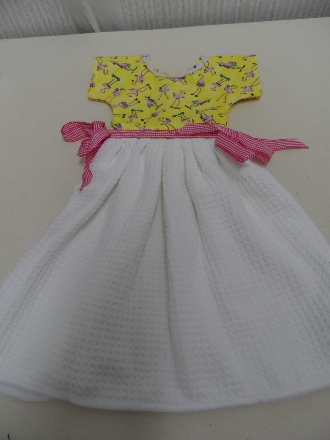 This is a dress made using a waffle weave towel, yellow quilt fabric with small flamingos on it, small white lace and pink gingham ribbon.  It has two sides so that it can hang over the oven door handle. This towel is also listed in my Etsy Shop.